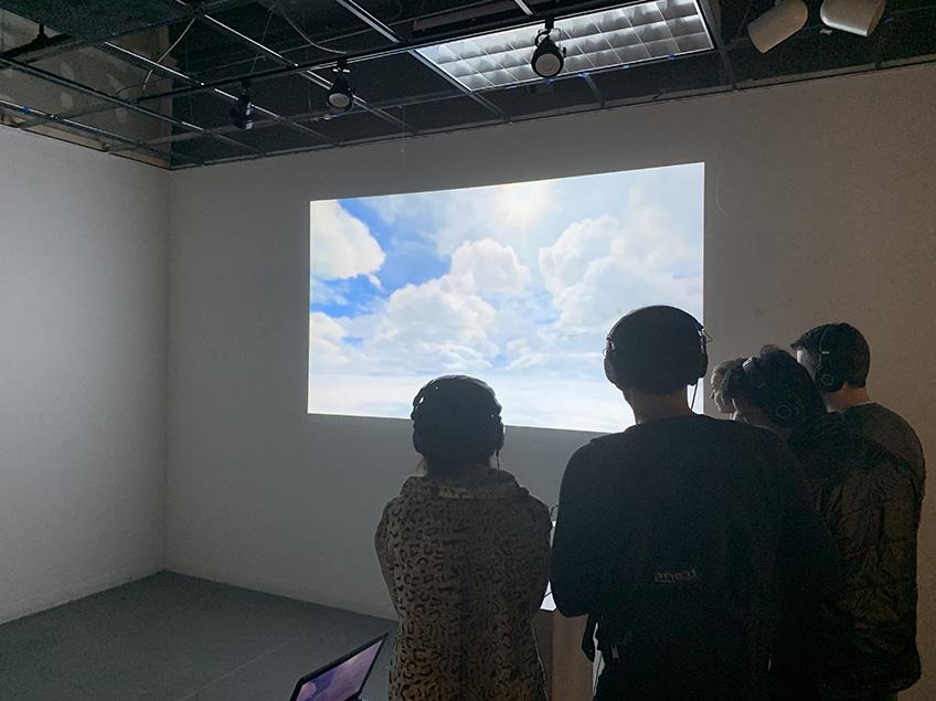 While wearing headphones, these four students are silhouetted against a projected image of the sky.